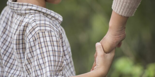 Close up of happy mum and son holding hand in a park. Family concept.